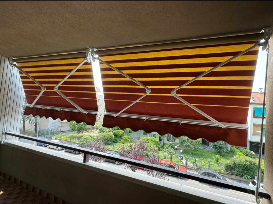 Tende da sole a righe rosse e gialle con bracci metallici, viste da un balcone.